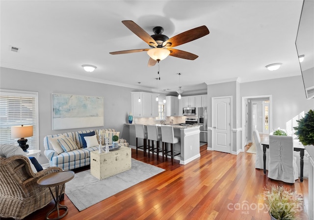 living room with ceiling fan, ornamental molding, visible vents, and light wood-style floors