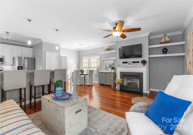 living area featuring light wood finished floors, a fireplace with flush hearth, and crown molding