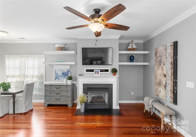 living area with crown molding, baseboards, wood finished floors, and a fireplace with flush hearth