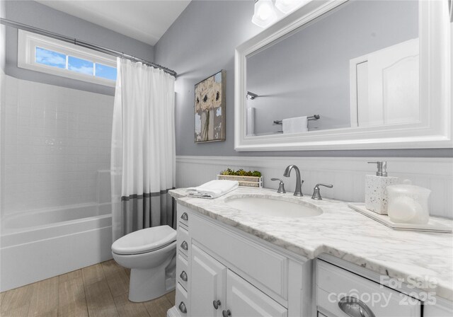 full bathroom with a wainscoted wall, toilet, vanity, and shower / bathtub combination with curtain