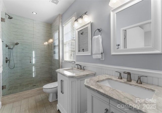 bathroom with two vanities, wainscoting, a sink, and a stall shower