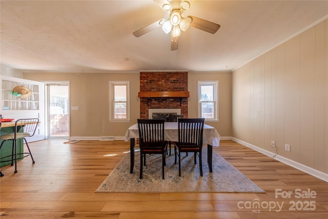 dining space with crown molding, a brick fireplace, ceiling fan, and light wood-type flooring