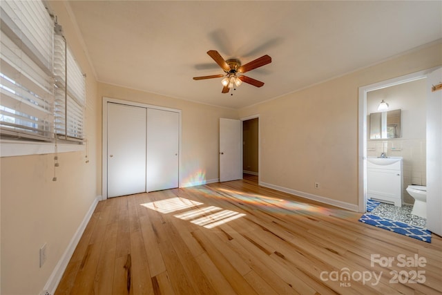 unfurnished bedroom with a closet, ornamental molding, ensuite bathroom, and light hardwood / wood-style flooring