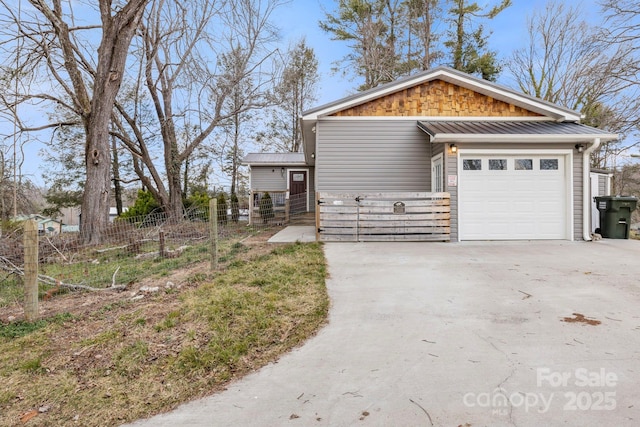 exterior space with fence, a standing seam roof, an attached garage, concrete driveway, and metal roof