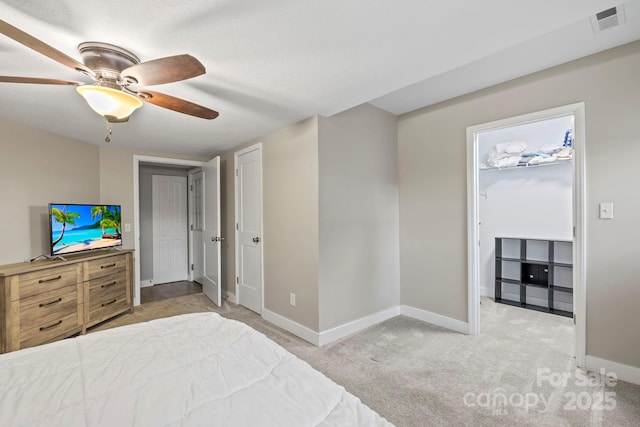 bedroom featuring ceiling fan, light carpet, and a walk in closet