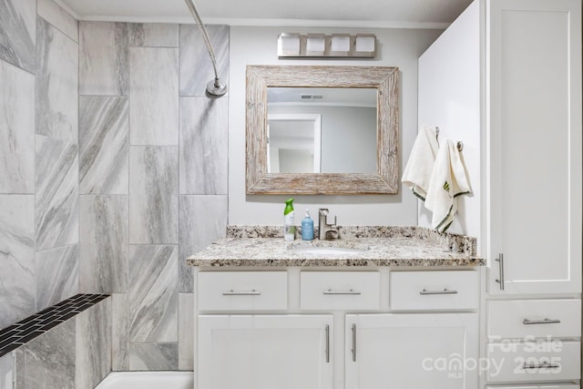 bathroom with ornamental molding, vanity, and tiled shower