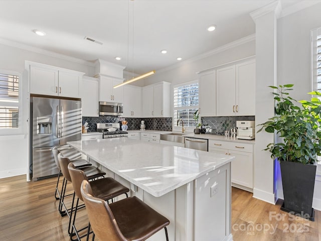 kitchen featuring appliances with stainless steel finishes, white cabinetry, a breakfast bar area, hanging light fixtures, and a center island