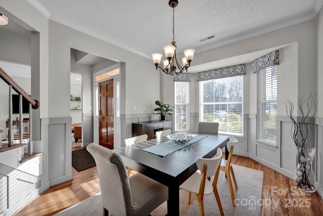 dining area with crown molding, a chandelier, light hardwood / wood-style floors, and a textured ceiling