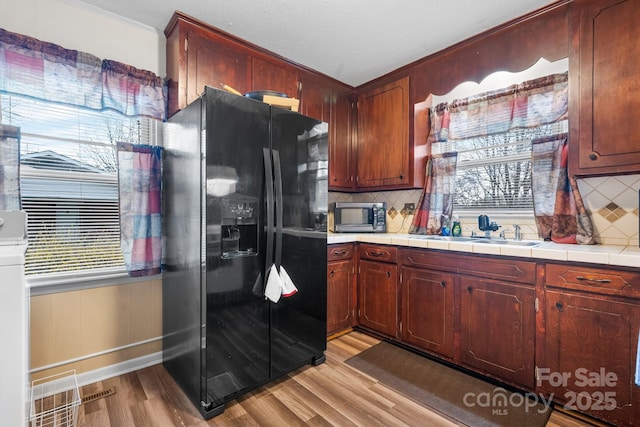 kitchen featuring stainless steel microwave, black fridge with ice dispenser, light wood-type flooring, and a sink