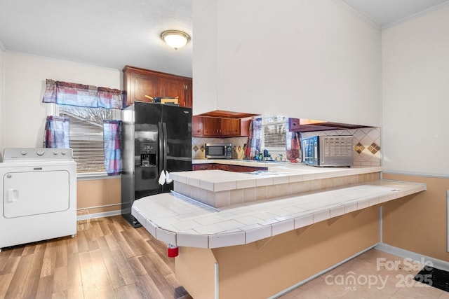 kitchen with washer / dryer, tile counters, stainless steel microwave, backsplash, and black fridge