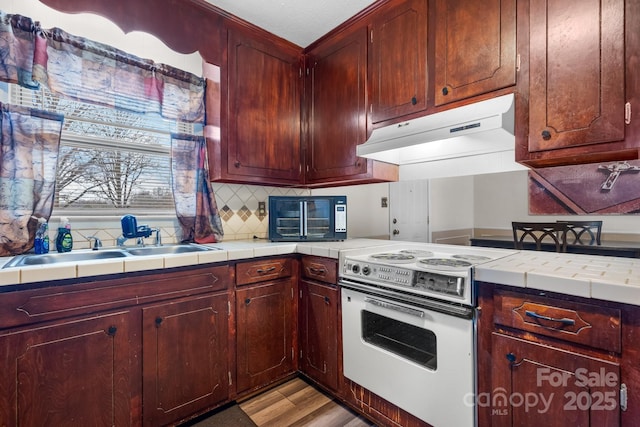 kitchen with electric stove, under cabinet range hood, a sink, tasteful backsplash, and light wood-style floors