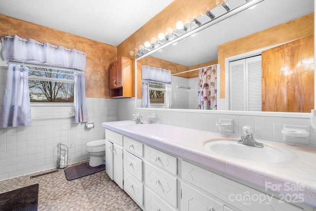 bathroom featuring curtained shower, toilet, tile walls, and a sink