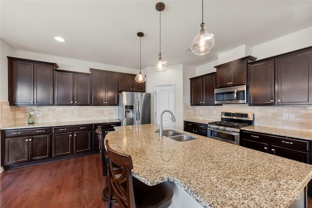 kitchen featuring sink, dark brown cabinets, hanging light fixtures, appliances with stainless steel finishes, and light stone countertops