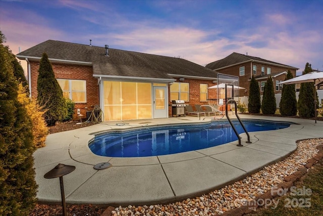 pool at dusk with a patio and area for grilling