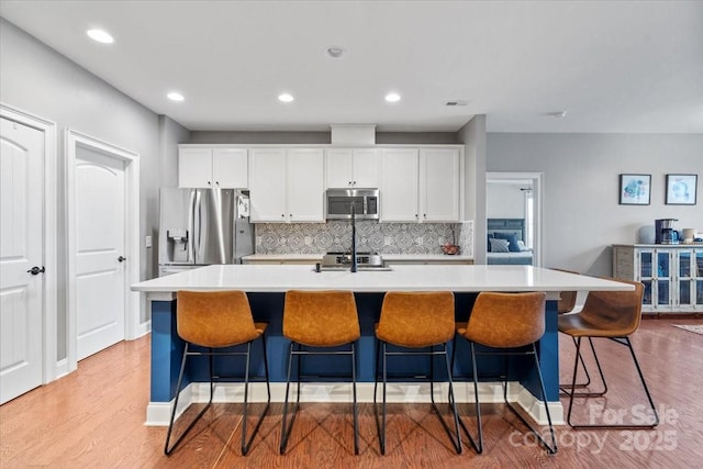 kitchen with stainless steel appliances, white cabinetry, a center island with sink, and a kitchen breakfast bar