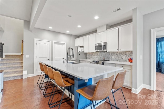 kitchen with a breakfast bar, an island with sink, sink, white cabinets, and stainless steel appliances