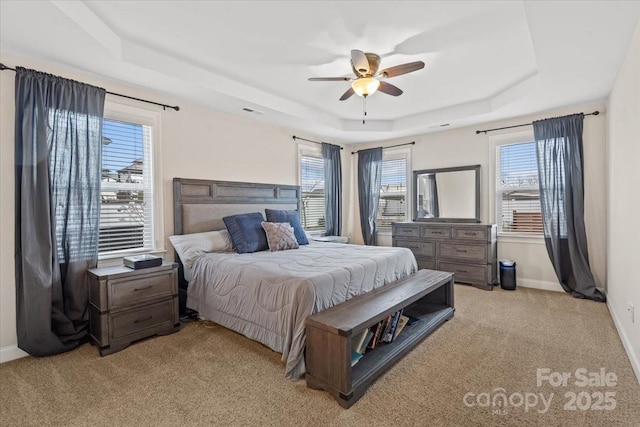 bedroom featuring a tray ceiling, light carpet, and multiple windows