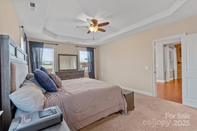 bedroom featuring ceiling fan, a tray ceiling, and light carpet