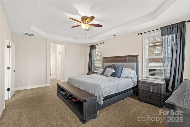 bedroom with multiple windows, carpet, ceiling fan, and a tray ceiling