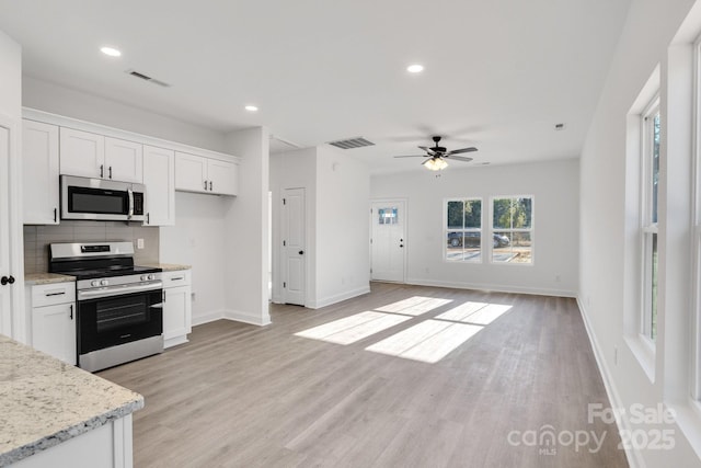 kitchen with appliances with stainless steel finishes, white cabinetry, backsplash, light hardwood / wood-style floors, and light stone countertops