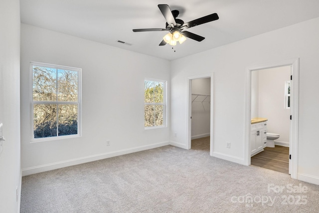 unfurnished bedroom featuring ensuite bathroom, a walk in closet, light carpet, a closet, and ceiling fan