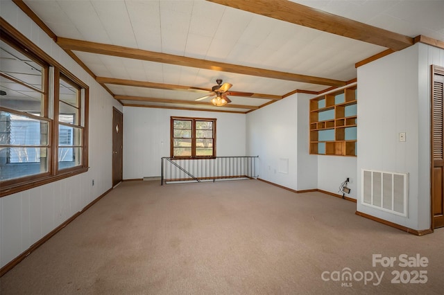 empty room with ceiling fan, carpet floors, and beamed ceiling