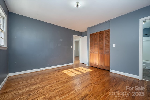 unfurnished bedroom with wood-type flooring, connected bathroom, and a closet