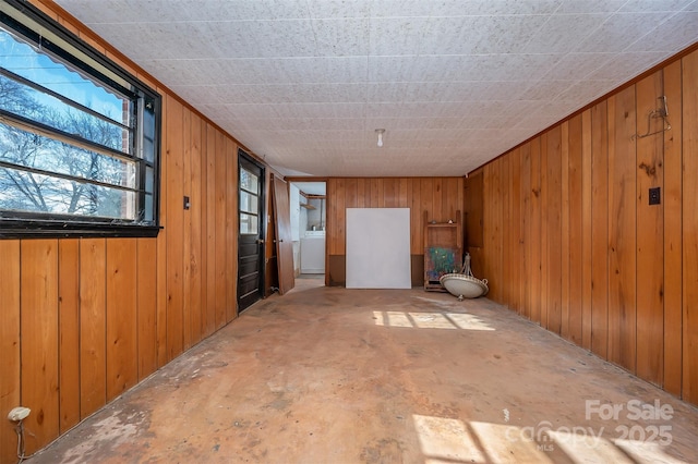 empty room featuring washer / clothes dryer, wooden walls, and concrete floors