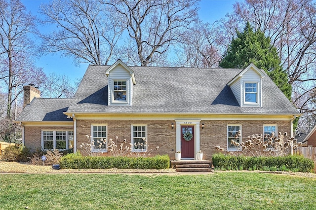 new england style home with a front yard, roof with shingles, and brick siding