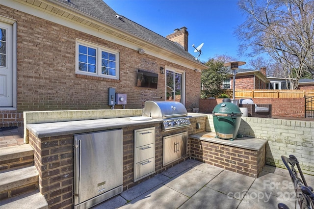 view of patio featuring a grill, fence, and an outdoor kitchen