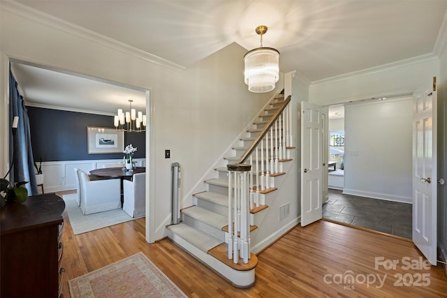 stairway featuring ornamental molding, wood finished floors, wainscoting, and an inviting chandelier