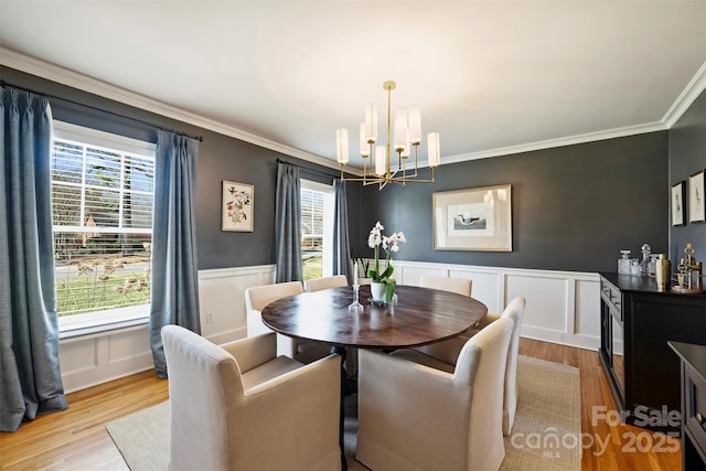 dining area with light wood-type flooring, crown molding, a notable chandelier, and wainscoting