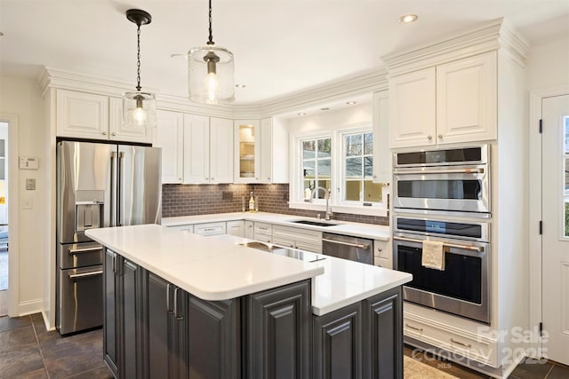 kitchen with tasteful backsplash, appliances with stainless steel finishes, white cabinets, a kitchen island, and a sink