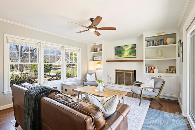 living room featuring built in shelves, a fireplace, ornamental molding, and dark wood-style flooring