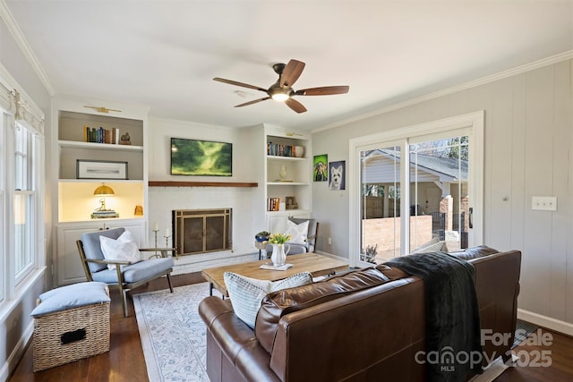 living room with built in shelves, a brick fireplace, crown molding, and wood finished floors