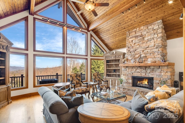 living room featuring a fireplace, beamed ceiling, ceiling fan, wood ceiling, and light wood-type flooring