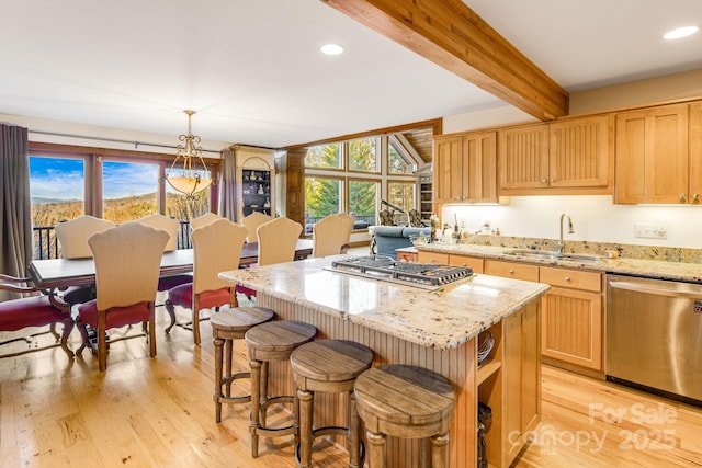 kitchen with appliances with stainless steel finishes, decorative light fixtures, sink, a center island, and light stone counters