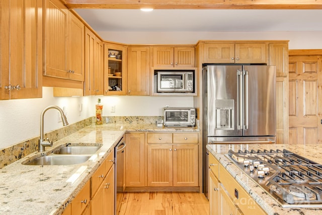 kitchen featuring light wood finished floors, a toaster, a sink, light stone countertops, and appliances with stainless steel finishes