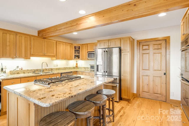 kitchen with a kitchen breakfast bar, a sink, beamed ceiling, a kitchen island, and appliances with stainless steel finishes