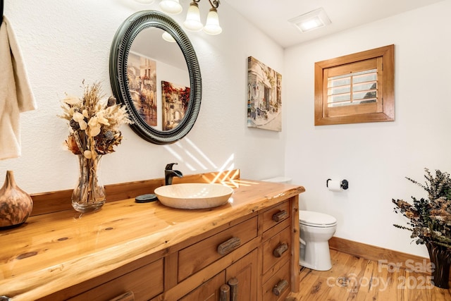 bathroom with baseboards, wood finished floors, vanity, and toilet