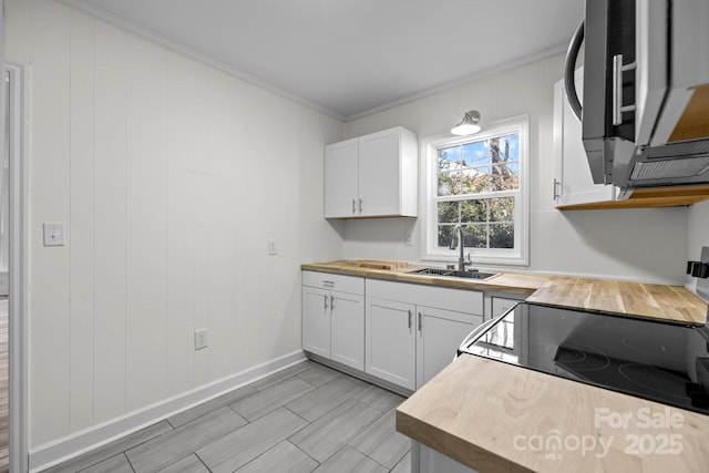 kitchen with white cabinetry, ornamental molding, butcher block counters, and sink