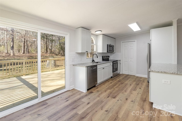 kitchen featuring appliances with stainless steel finishes, sink, white cabinets, light stone counters, and light hardwood / wood-style floors