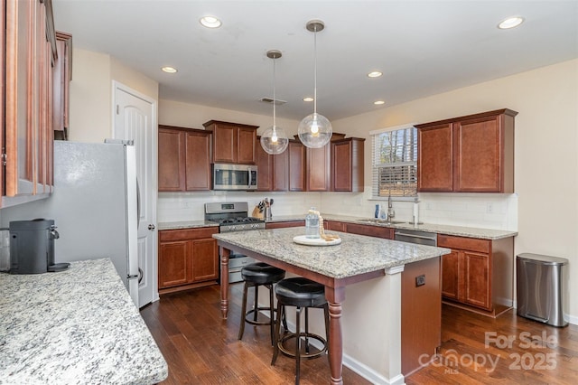 kitchen featuring pendant lighting, stainless steel appliances, light stone countertops, and a kitchen island