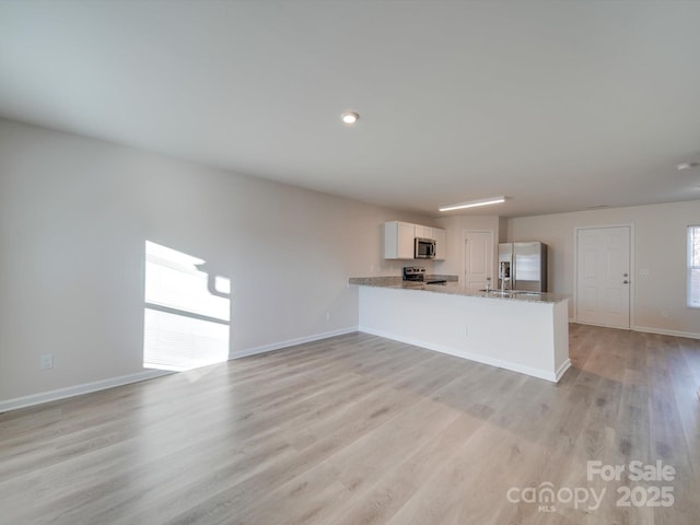 kitchen with white cabinetry, light stone counters, light wood-type flooring, kitchen peninsula, and stainless steel appliances