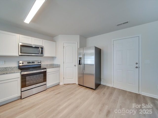 kitchen with white cabinetry, stainless steel appliances, light stone counters, and light wood-type flooring