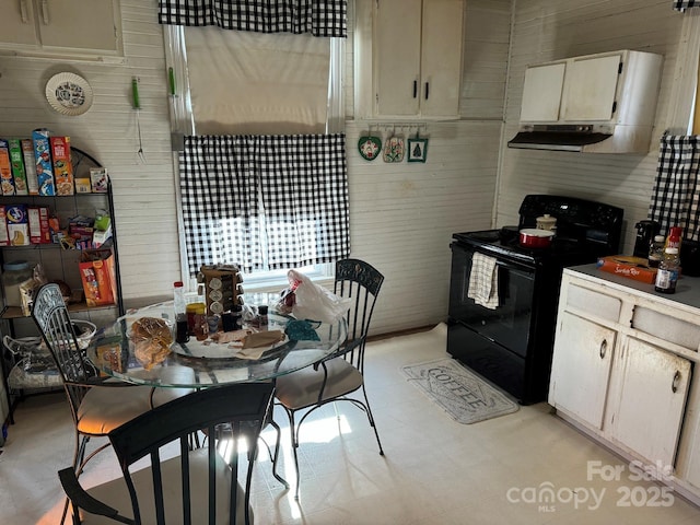 kitchen featuring wood walls, black range with electric stovetop, and cream cabinetry