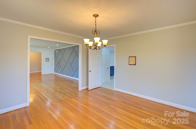 empty room with ornamental molding, a chandelier, and light hardwood / wood-style flooring