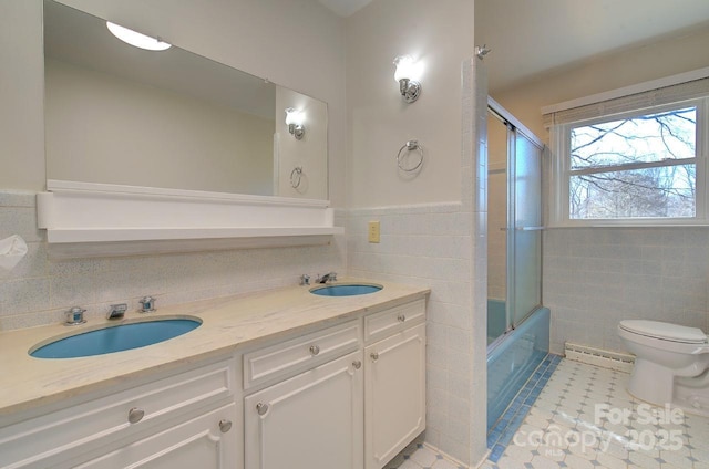 full bathroom with tile walls, bath / shower combo with glass door, vanity, tile patterned floors, and toilet