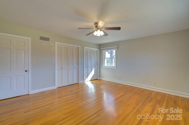 unfurnished bedroom with ceiling fan, light hardwood / wood-style floors, and two closets