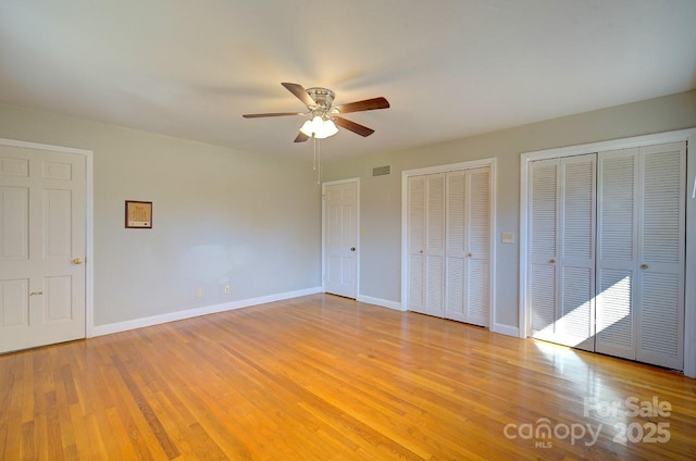 unfurnished bedroom featuring multiple closets, ceiling fan, and light wood-type flooring